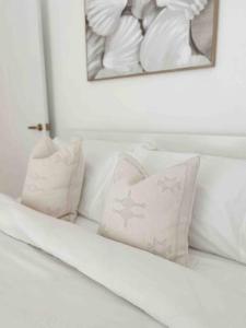 een wit bed met kussens en een foto aan de muur bij The Summer House in Long Jetty