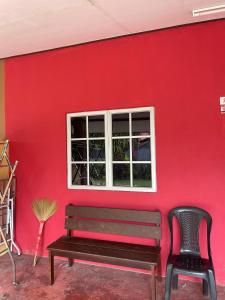 a red wall with a bench and a window at Teratak Atok Ajib in Pantai Cenang