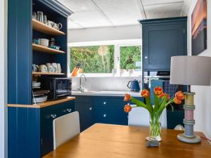 eine Küche mit blauen Schränken und einem Tisch mit Blumen darauf in der Unterkunft Little Palms in Bude