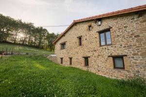 a stone house with a green field next to it at The Stone House naturaleza y confort in Santibáñez de Villacarriedo
