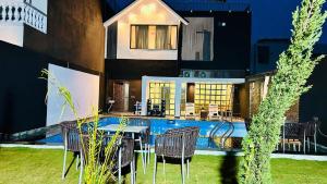 Black Rose 5 BHK Premium Luxurious villa في Nāi: فناء مع طاولة وكراسي بجوار حمام السباحة