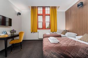 a hotel room with a bed and a desk and a bed and yellow curtains at Pałac nad Jeziorem in Chociwel