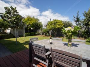 a wooden table with a bottle of wine and a vase of flowers at Fabulous In Fitzroy - seconds to Fitzroy Beach in New Plymouth