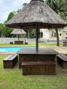 a table with a straw umbrella and benches next to a pool at Eden Wilds 42 in Port Edward