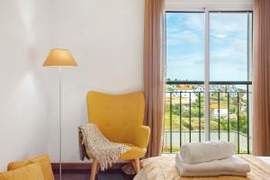 a bedroom with a yellow chair and a window at Casa Nóbrega in Caniço