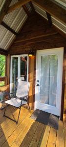 a white chair sitting on a porch with a door at Tree House Glamping Destination near the Ozarks, with River Access for Swimming and Fishing in West Liberty
