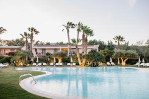 a large swimming pool with palm trees and a building at Hotel Aquadulci in Chia