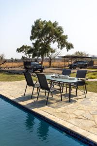 ein Tisch und Stühle neben einem Swimmingpool in der Unterkunft Rain Tree Camp in Chunga