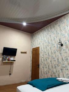 a room with a bed and a tv and a wall at Sapo Guest House in Berastagi
