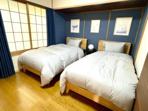 2 Betten in einem Zimmer mit blauen Wänden und Fenstern in der Unterkunft The Black Wolf in Hakuba