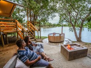 three people sitting around a fire pit next to a lake at AfriCamps Hoedspruit in Hoedspruit