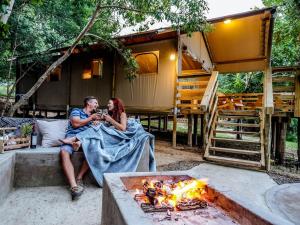 a man and a woman sitting on a bed in front of a house at AfriCamps Hoedspruit in Hoedspruit