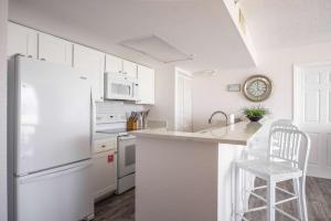a white kitchen with a white refrigerator and a stool at Tortuga Suite at Sunrise Suites Resort - Heated Pool, Hot Tub & Free Parking in Key West