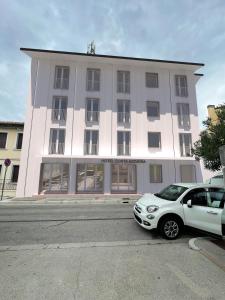 Un edificio blanco con un coche aparcado delante. en Hotel Costa Azzurra, en Grado