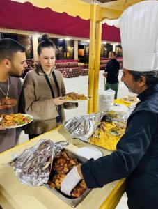 DisahRUM ROYAL CLASSIC lUXURY CAMP的一名戴着厨师帽的男子正在柜台准备食物。