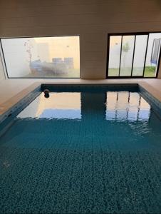 Una piscina con agua azul en una habitación con ventanas. en شاليه داله العماريه2 بالكامل لك وأجواء ممتعه, en Al ‘Ammārīyah