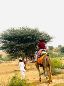 a man riding a horse in the desert with a man walking at HP Desert Luxury Camp in Jaisalmer