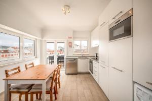 a white kitchen with a wooden table and chairs at GuestReady - Sunny Retreat in Costa da Caparica in Costa da Caparica