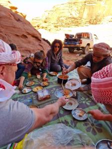 ワディ・ラムにあるMars moon campのテーブルの周りに座って食事をとる人々のグループ