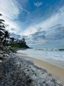 a beach with rocks and the ocean on a cloudy day at Lima Beach House Varkala in Varkala