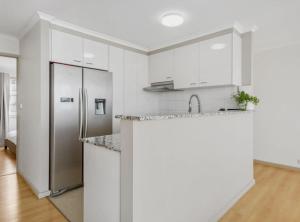 a kitchen with white cabinets and a stainless steel refrigerator at 2-Bed Unit with Balcony BBQ & Stunning Lake Views in Belconnen