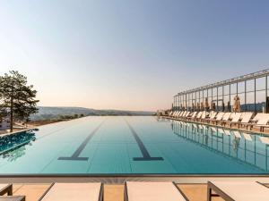 维尔蒂尼克Movenpick Resort and Spa Fruske Terme的一座建筑物边带椅子的游泳池
