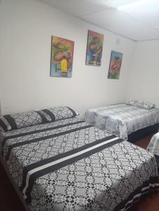 two beds in a room with paintings on the wall at Hostal Y Hospedaje Familiar Amanecer del Valle 1 in Valledupar