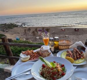 a table with plates of food on the beach at Atlantique Assilah Vue Mer, Piscines, Clim & Wi-Fi in Asilah