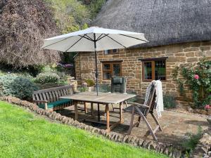 ein Picknicktisch mit Sonnenschirm und Bank in der Unterkunft Fairytale Cottage in the Country in Hornton