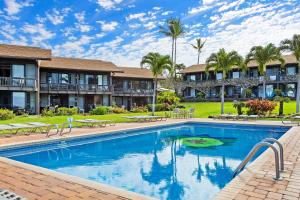 a swimming pool in front of a resort with palm trees at Mahina Surf 117 in Kapalua