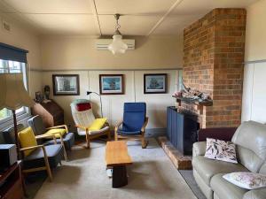 a living room with a couch and chairs and a brick fireplace at The Cottage at Raheen in Mallacoota