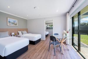 オークランドにあるAlbany Oak Motelのベッド2台とガラスのテーブルが備わるホテルルームです。