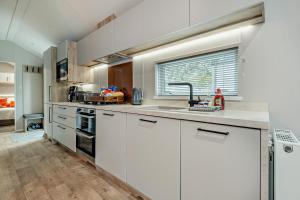 a kitchen with white cabinets and a sink and a window at Astoria Lodge Smart Modern 2-Bedroom Holiday Lodge Milford on Sea in Milford on Sea