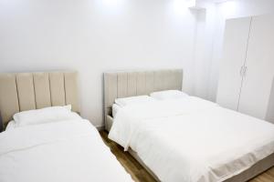 two beds in a bedroom with white walls and wood floors at The Central Spot in Tirana