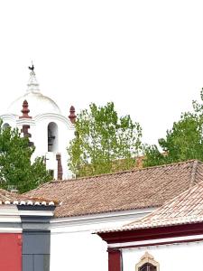 eine weiße Kirche mit einem weißen Turm hinter einigen Dächern in der Unterkunft Casa da Vila Messines in São Bartolomeu de Messines