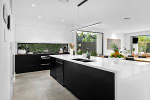 Nalu Beach House - Kingscliff Getaway by uHoliday في كينغسكليف: مطبخ مع دواليب سوداء وقمة بيضاء