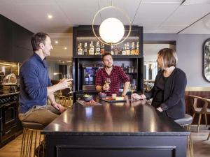 a group of three people sitting around a bar at Mercure Nancy Centre Place Stanislas in Nancy