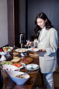 Una mujer con traje blanco preparando comida en una mesa en Vogue hotel, en Almaty 24 fotos más