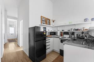 uma cozinha com um frigorífico preto e armários brancos em Bespoke Stays - Rustic Stanley Bay Apartment em Auckland