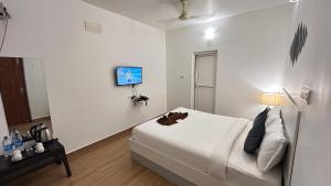 a white room with a bed and a tv on the wall at The Base Inn in Puducherry