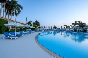 a large swimming pool with chairs and palm trees at JAZ Royal Palmariva in Hurghada