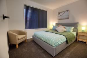 a bedroom with a bed and a chair and a window at Sorell Gateway Villa in Sorell