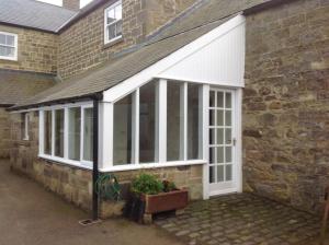 una extensión a una casa de ladrillo con salón acristalado en The Old Post Office B&B, en Longwitton