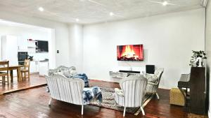 a living room with white chairs and a piano at Jacaranda Escape 4 x King Bed 3 Bath House in Pretoria
