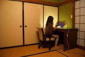 een vrouw aan een bureau met een laptop bij ゲストハウス灯 in Azumino