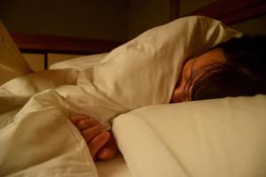 een persoon die in bed ligt onder een deken bij ゲストハウス灯 in Azumino