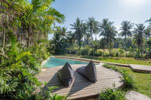 een houten terras met kussens naast een zwembad bij Emana Bambooscape in Ubud
