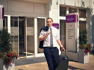 グラーツにあるホテル メルキュール グラーツ シティのスーツケースを持って建物の前を歩く男