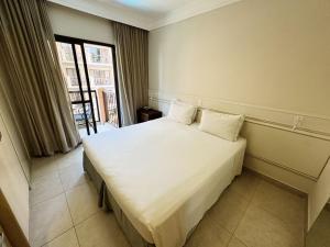 Un dormitorio con una gran cama blanca con ventana. en Destino Floripa Jurerê, en Florianópolis