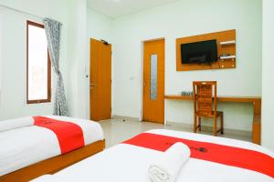 two beds in a room with a tv and a desk at RedDoorz Plus @ Mahendradatta Denpasar in Denpasar +40 photos